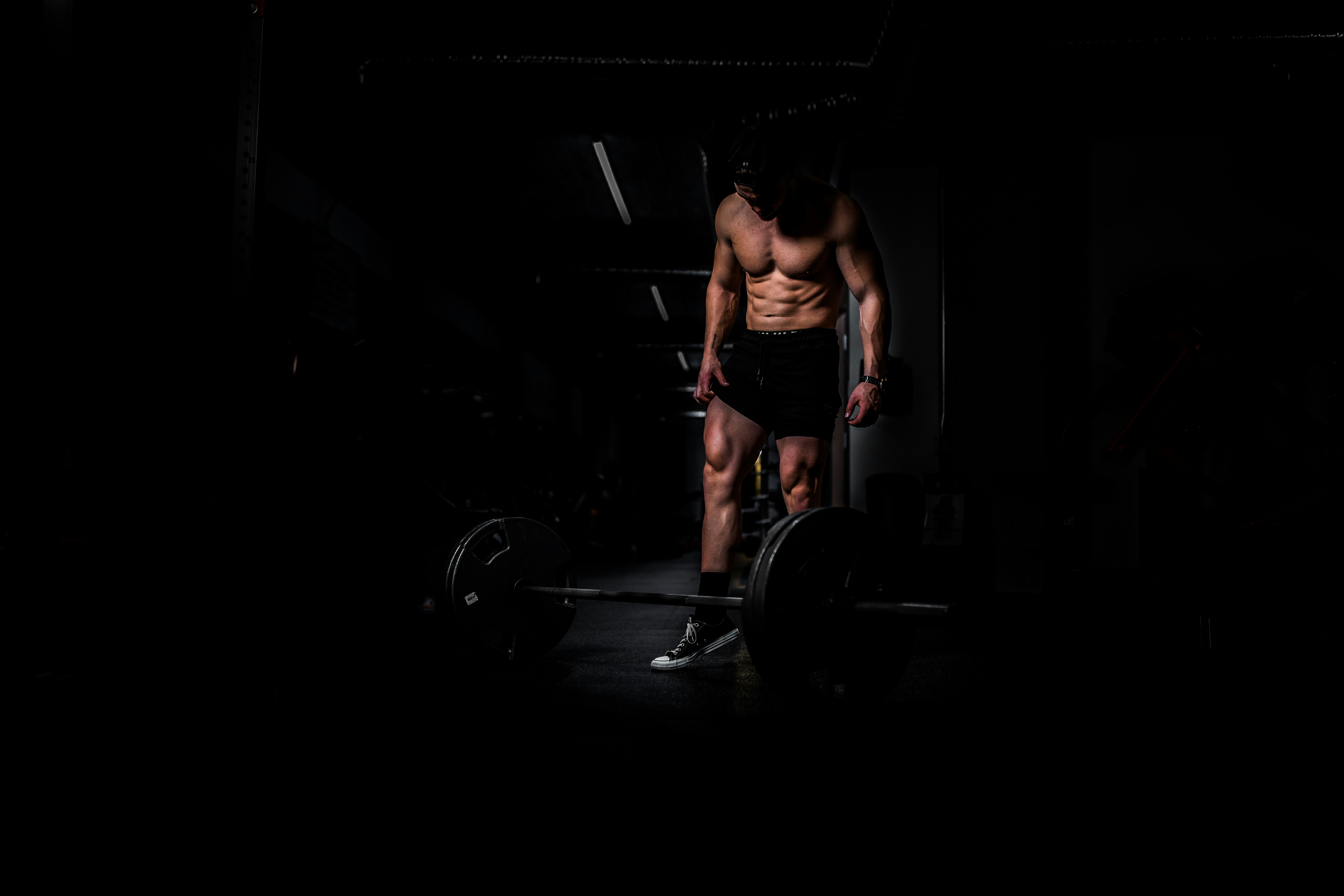 Lifter standing over a barbell in a dark gym preparing for a heavy set